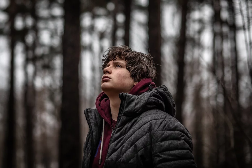 Portrait d'un garçon qui regarde le ciel dans la forêt sombre