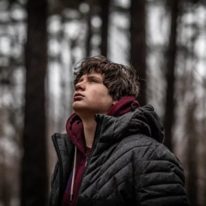 Portrait d'un garçon qui regarde le ciel dans la forêt sombre