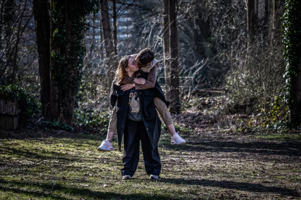 Deux femmes sont dehors. L'une d'elle porte l'autre sur son dos et elles s'embrassent. Elles semble être dans un parc.